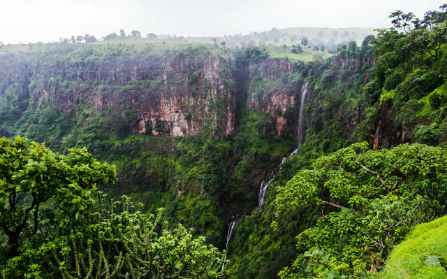 A monsoon-green gorge with a thin waterfall dropping down red basalt cliffs at Toranmal, Nandurbar district, Maharashtra.